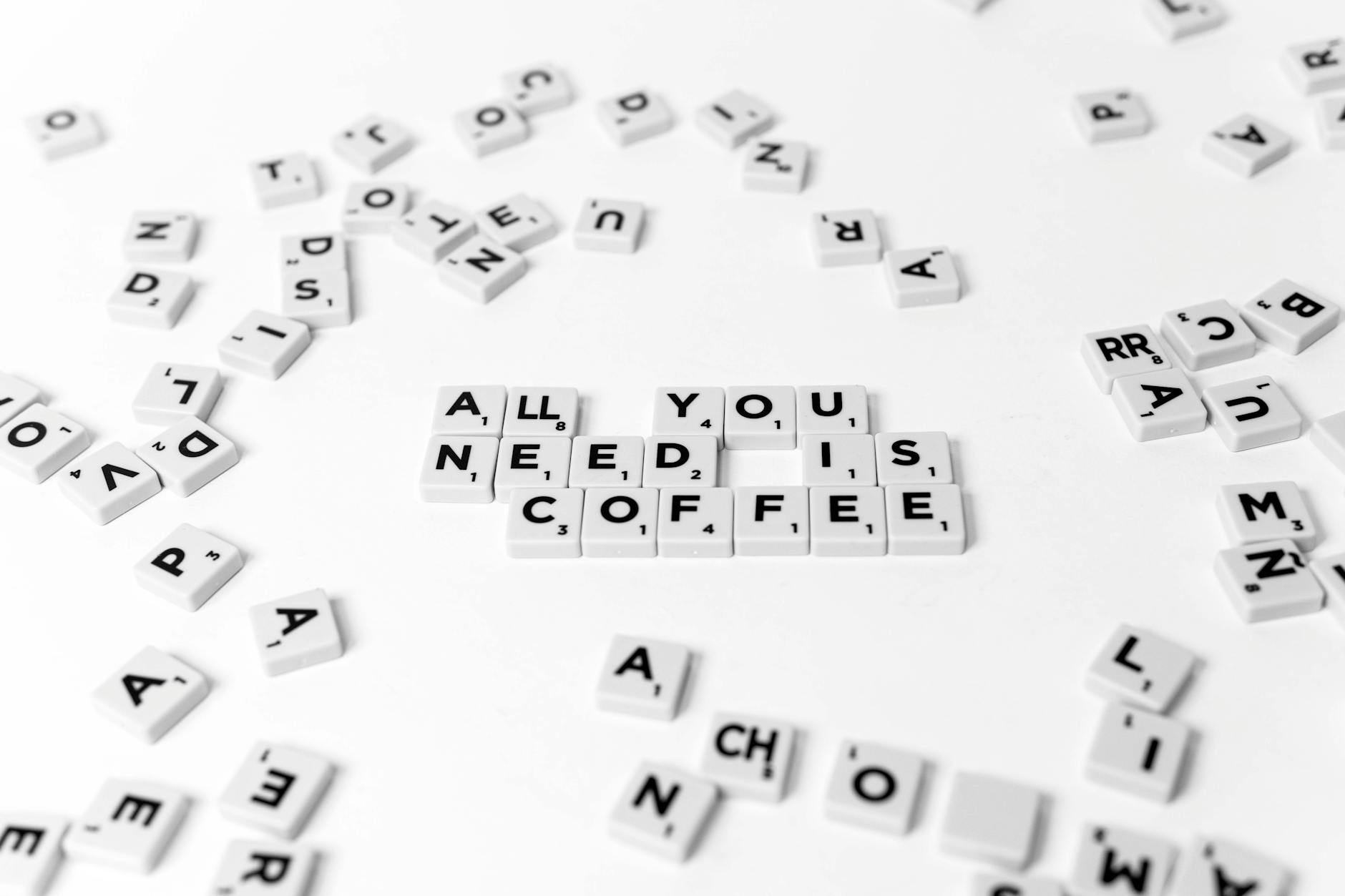 Scrabble tiles spell out 'All You Need Is Coffee' on a white background, offering a creative still life.