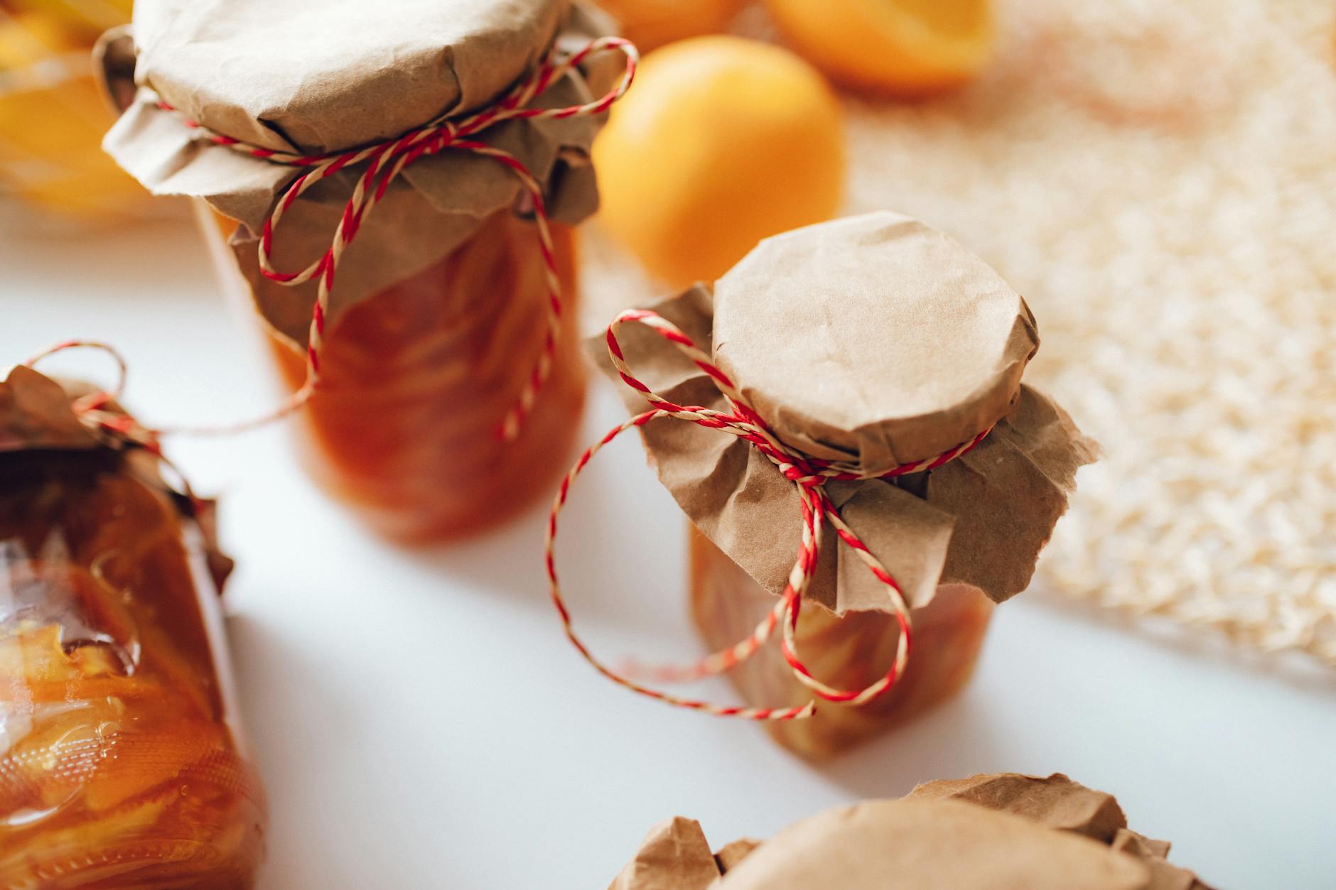 A close-up image of homemade preserves in jars wrapped with paper and string, indoors.