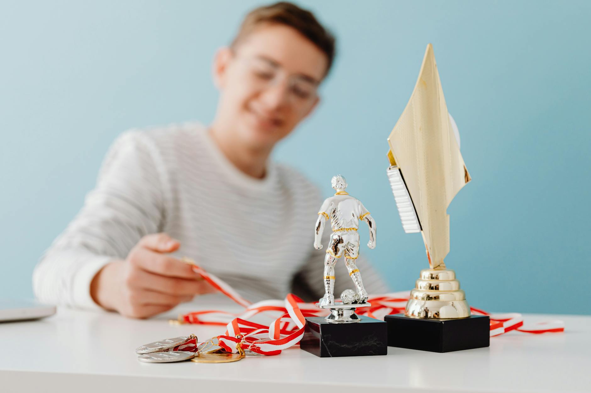 Teenage boy sitting with soccer trophy, medals, and award cup, smiling.